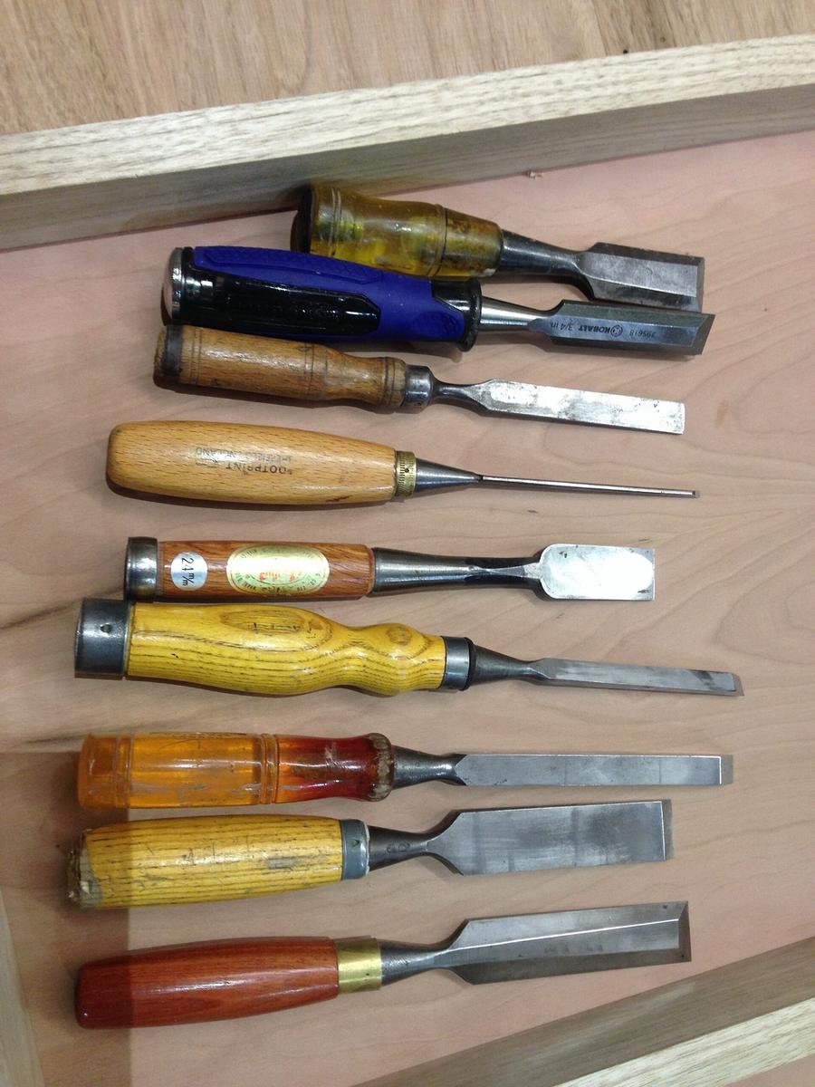 Een rij beitels met houten handvatten, van smal naar breed, op een werkbank