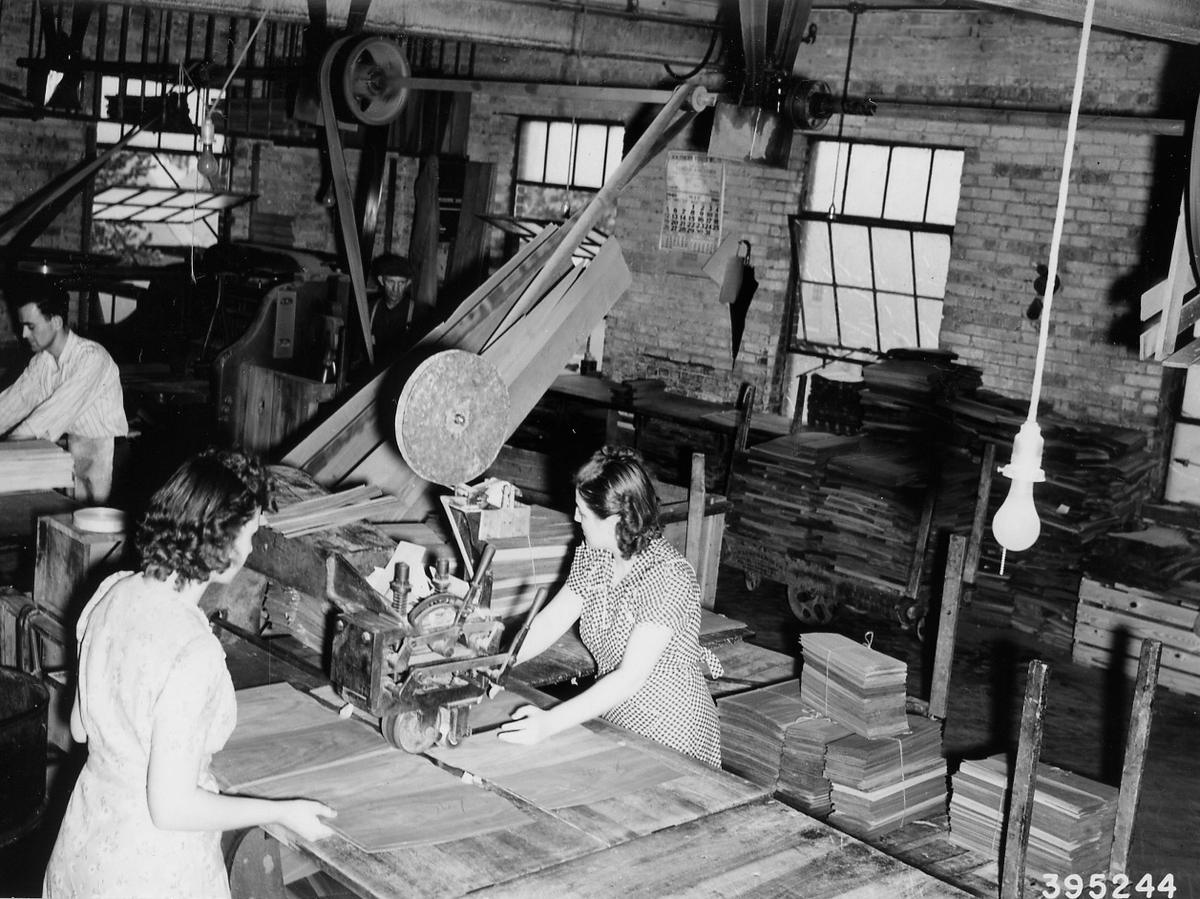 Twee vrouwen voeren fineerstroken door een machine in een houtfabriek